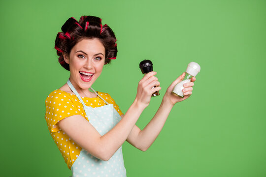 Photo of pretty cute girlish young lady roller hairstyle hold pepper shaker salt bottle open mouth pretend mexican dancer wear dotted apron shirt isolated green color background