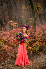 Beautiful young woman in a wreath and a bouquet of flowers in an autumn park. Girl with beautiful floristry.