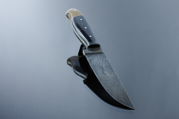 an all-metal, middle kitchen knife lies on a mirror surface, a blade made of multilayer damask...