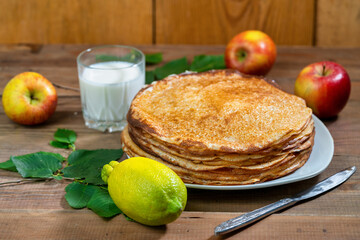 Apples, lemon, sour cream and pancakes on a plate on a wooden table