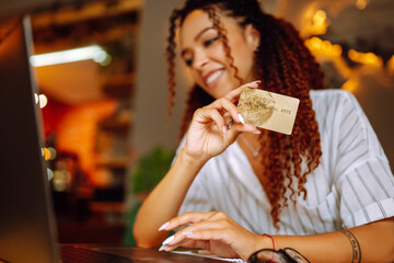 Сredit card in female hand. African American woman sitting at cafe making online shopping. Online shopping, e-commerce, internet banking, spending money.