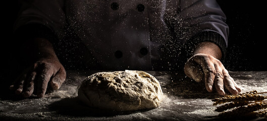 Chef hands cooking dough on dark wooden background. White flour flying into air. Food concept