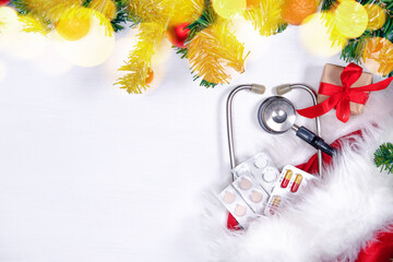 Medical banner with pills, gift present box, stethoscope and Christmas tree on white wooden background. Copyspace. Medicine new year flatly.