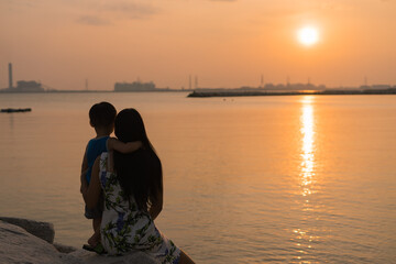 Mother and son in a deep moment of love during sunset on the sea shore and child hugging mother. - Concept of union and tender connection between a young mother and his lovely child.