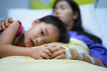 Woman patients lying on bed in hospital. Hands with saline solution. Her hand is held by her son's hand for encouragement.