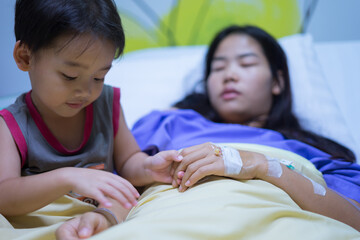 Woman patients lying on bed in hospital. Hands with saline solution. Her hand is held by her son's hand for encouragement.