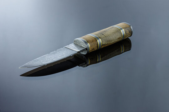 handmade carving knife on a mirrored surface, damascus blade, wood handle and damask steel spacers