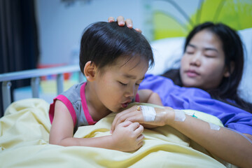 Woman patients lying on bed in hospital. Hands with saline solution. Her hand is held by her son's hand for encouragement.