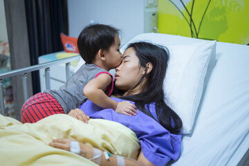 Woman patients lying on bed in hospital. Hands with saline solution. Her hand is held by her son's hand for encouragement. She hugged and kissed her son.