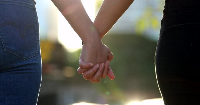 Close-up of hands joining together with sunlight flare in the background. Beautiful romantic moment between two lovers