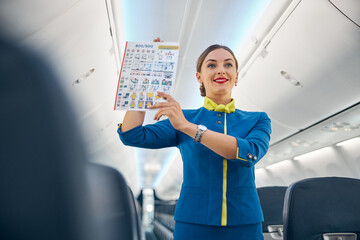 Smiling cheerful air hostess in blue uniform showing to passenger safety information
