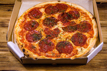 Pizza with salami sausage and parmesan cheese in cardboard box on a wooden table