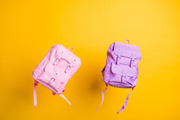 Pink and purple school bags flight over yellow color background shopping center offer low prices study supplies