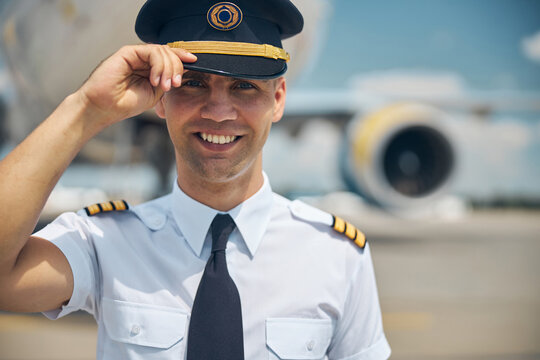 Handsome pilot in command touching captain hat and smiling