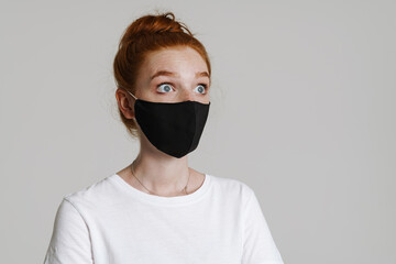 Image of shocked ginger girl in face mask posing and looking aside