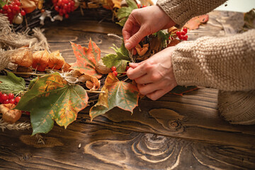 Making a wreath of autumn leaves and natural materials on rustic wooden boards.