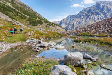 Fototapeta na wymiar Idyllic summer landscape with hiking trail in the mountains with beautiful fresh green mountain pastures, river with reflection and clouds.
