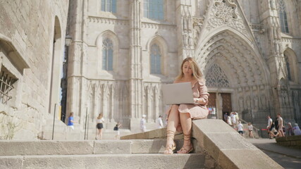 Fototapeta na wymiar Laughing woman working with laptop near cathedral. Smiling girl getting message
