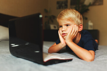 child does homework , lying in bed using his laptop or skyping.