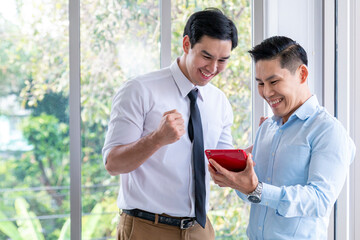 Mature businessman using a digital tablet to discuss information with colleague. Two young businessmen using touchpad at meeting. Cheerful businessmen standing and using tablet in office together.