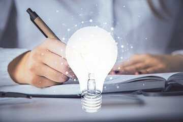 Bulb hologram over hands taking notes background. Concept of idea. Double exposure