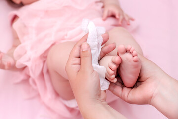 Hygiene - young mom wiping the baby skin body and face with wet wipes carefully on pink background....