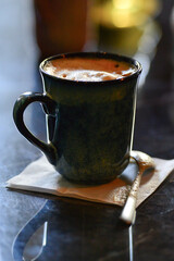 A mug of coffee with foam is on a napkin on the table.