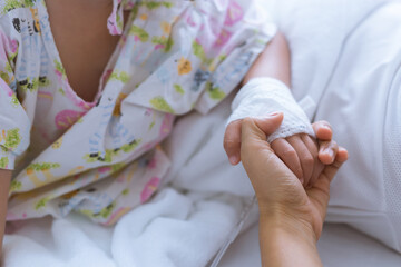 Hands of mother and sick Asian little boy holding together on sickbed in hospital to give encouragement. Healthcare medical.