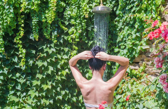 young woman from behind showering outdoors in a garden with plants
