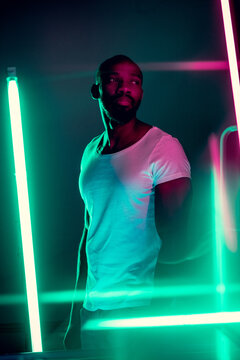 Geometric lines. Cinematic portrait of stylish young man in neon lighted room. Bright neoned colors. African-american model, musician indoors. Youth culture in party, festival style and music concept.