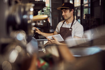 Handsome young man controlling work of coffee roasting machine