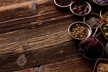 Natural medicine background. Assorted dry herbs in bowls and brass mortar on rustic wooden table.