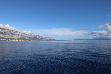 Seascape on the Croatian coast view from the sea on a sunny day. A scenic view of the coastline of the mountain range and island against the backdrop of the blue sea and clear sky on a September day