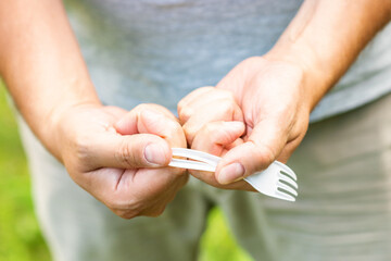 Male hands breaks plastic disposable fork in the park. The concept of environmental problems. Plastic free