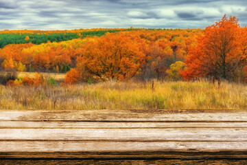 Empty wooden table with blurred picturesque autumn landscape of panoramic view from hill to lowland with field and grove in cloudy day. Mock up for display or montage products