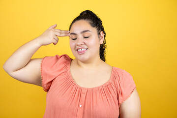 Young beautiful woman with curly hair over isolated yellow background hooting and killing oneself pointing hand and fingers to head like gun, suicide gesture.