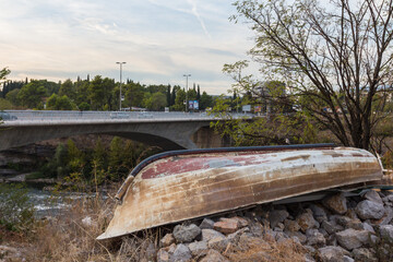 An old boat lies on the river on the background of the bridge in Pogorica. Montenegro