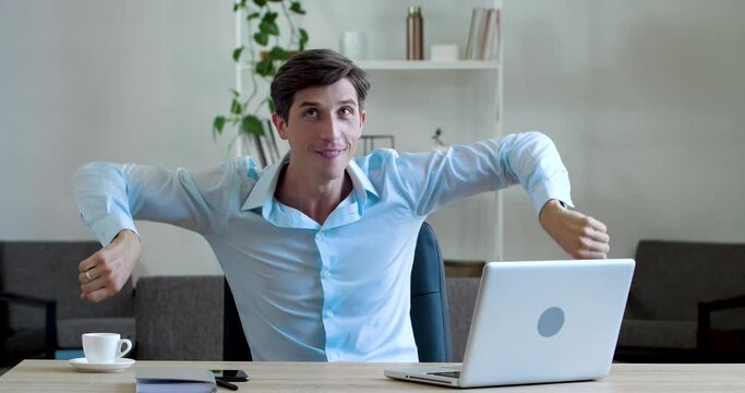 Active funny young business man manager doing exercises in office sitting at table, actively moving his arms, twirling hands, dancing at work during break having fun, doing gymnastics for male body