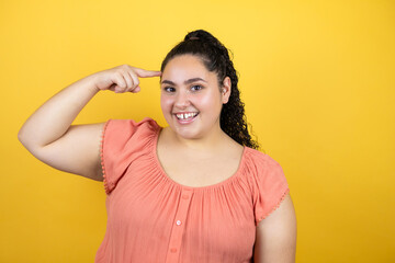 Young beautiful woman with curly hair over isolated yellow background smiling and thinking with her fingers on her head that she has an idea.
