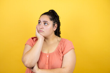 Young beautiful woman with curly hair over isolated yellow background thinking looking tired and bored with crossed arms