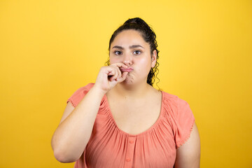 Young beautiful woman with curly hair over isolated yellow background mouth and lips shut as zip with fingers. Secret and silent, taboo talking