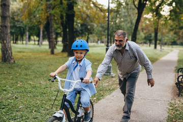 Fototapeta premium boy riding bicycle with his grandfather at the city park