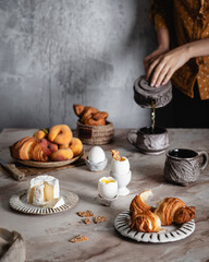 soft boiled eggs, fresh cheese and croissants on marble background, fresh peaches, cup of tea, selective focus, traditional breakfast concept