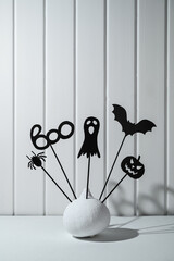 Halloween home decorations. Painted white pumpkin and black Halloween scary shadow puppets on sticks against a white wooden wall. Copy space, vertical orientation.