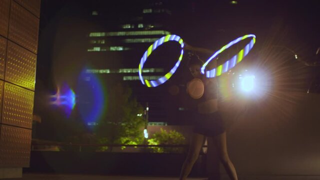 Sporty woman exercising with illuminated hula hoops in city at night