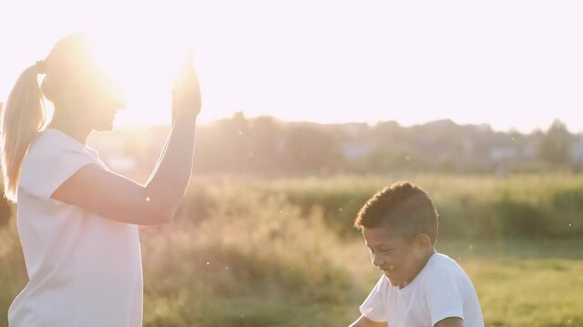 A happy mother is having fun with her son. The kid is holding mother's hands. Sunset. Happy family concept.