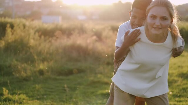 A happy mother is having fun with her son. The kid is at mother's back smiling. Sunset. Happy family concept.