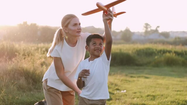 Happy kid and woman playing with toy airplane against field. The mother and son are having fun on summer sunset .