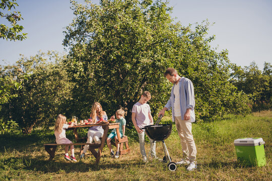 Full length photo big family five people three small children dad make fried sausage mom talk kids wait meat breakfast table relax sunny day house green park fenced backyard outside outdoors