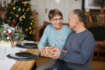 Senior couple exchanging christmas cifts sitting at the Christmas decorated table at home